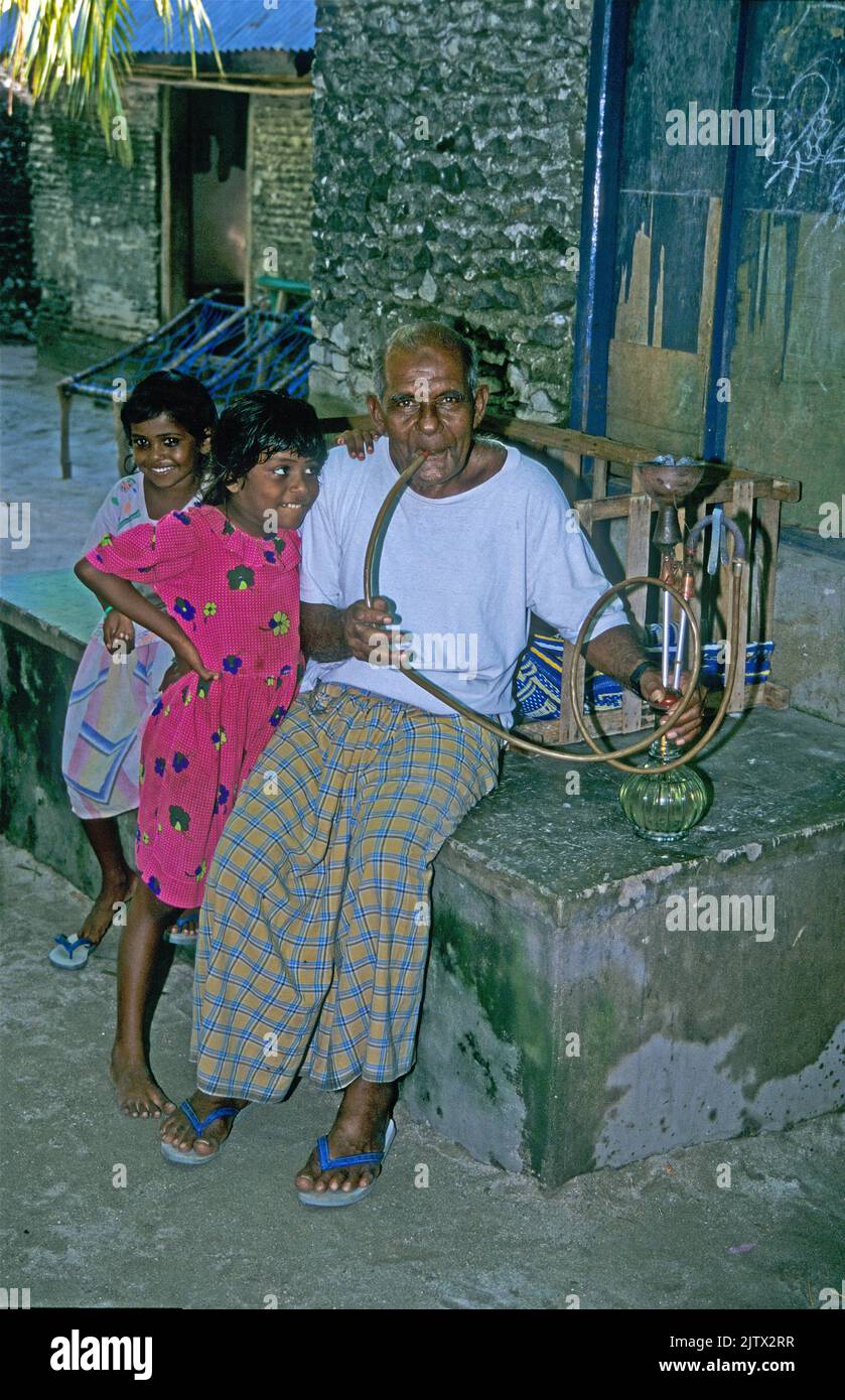 Junge Mädchen mit einem alten maledivischen Mann, raucht eine Wasserpfeife, Heimatinsel Mahembadhoo, Malediven, Indischer Ozean, Asien Stockfoto