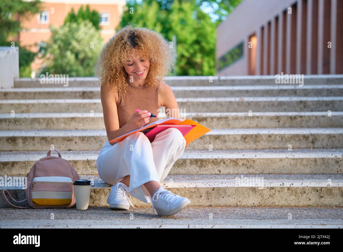 Junge brasilianische Universitätsstudentin, die mit einem Kaffee auf der Treppe sitzt. Stockfoto