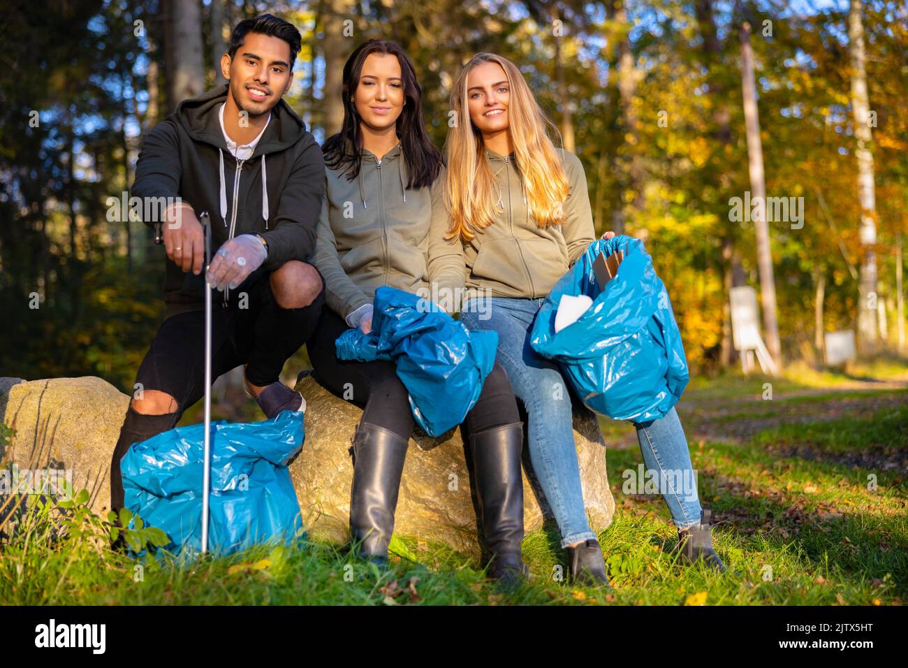 Multiethnische Freiwillige im Umweltschutzteam sitzen mit Müllsäcken Stockfoto