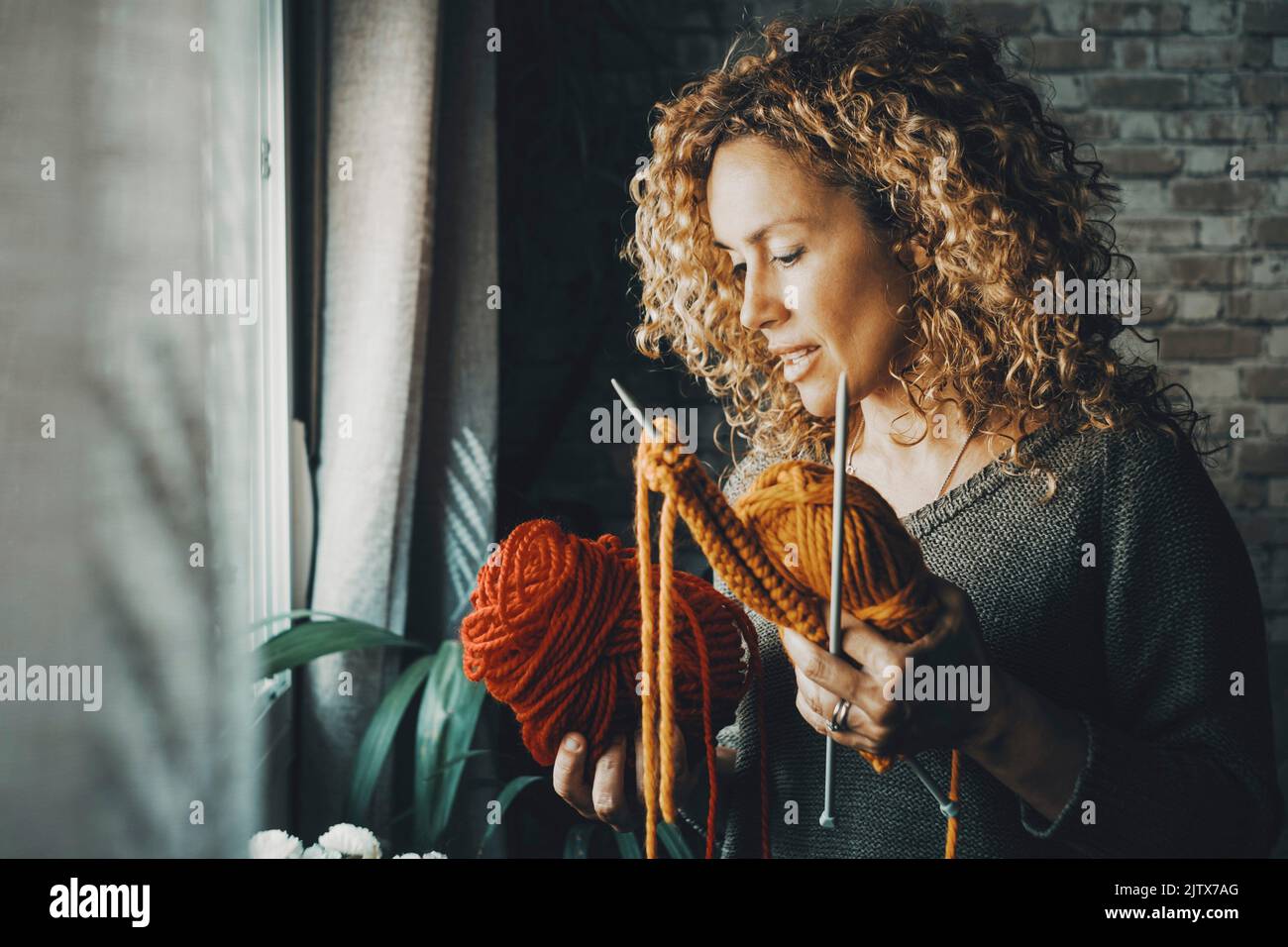 Porträt einer attraktiven Frau zu Hause in Indoor-Freizeitbeschäftigung mit Nadeln zu stricken Arbeit bunte Wolle. Weibliche Menschen und Hobbys. Junge Dame Stockfoto