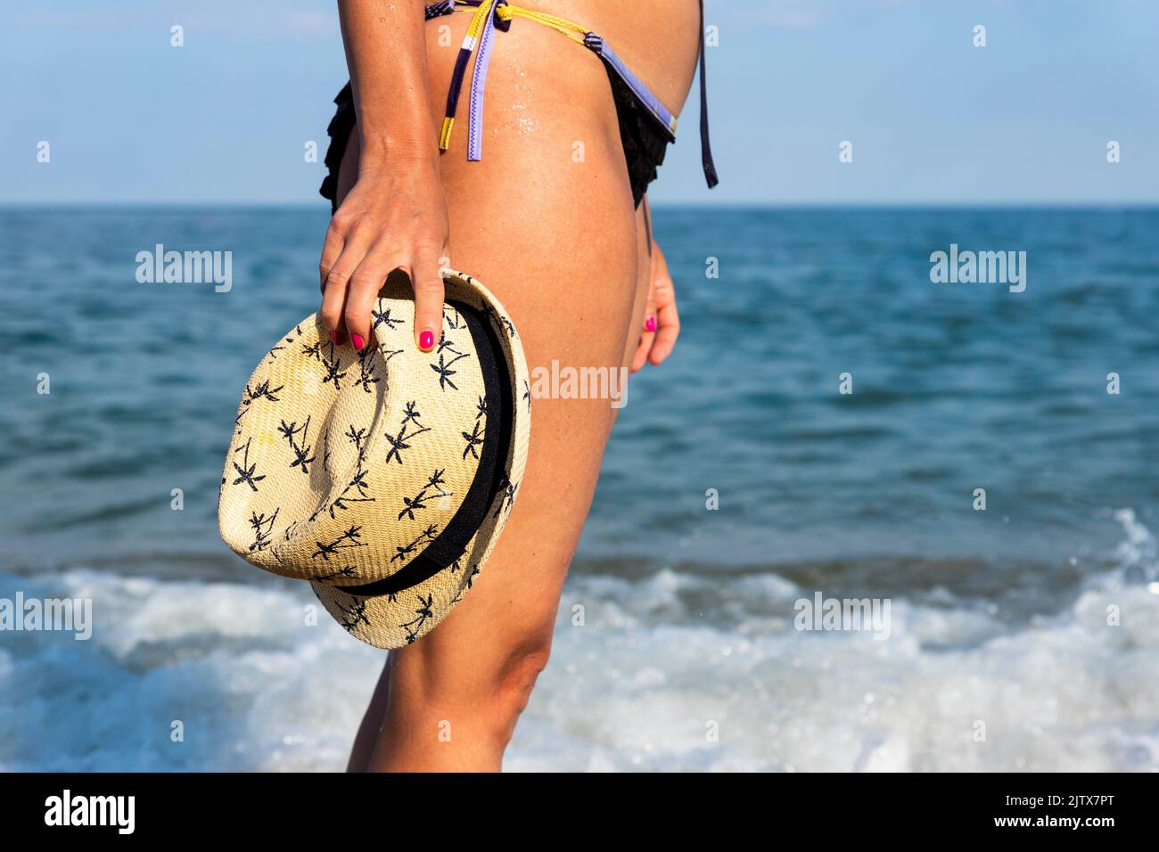 Frau im Bikini mit Strohsonnenhut am sonnigen Strand auf dem Meer. Reise- und Modekonzept. Stockfoto
