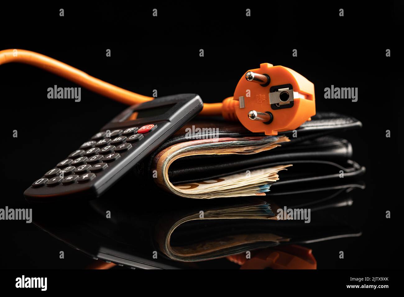 Orangefarbener Stecker, Geldbörse mit Geld und Taschenrechner auf schwarzem Hintergrund. Konzept der steigenden Strompreise. Stockfoto