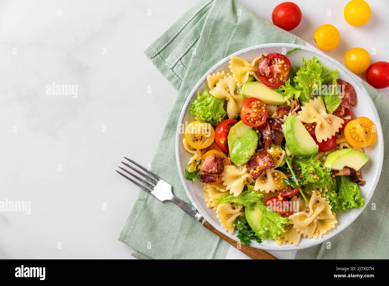Kalter Sommer-Nudelsalat mit Speck, Tomaten, Avocado und Senf auf einem Teller mit Gabel auf weißem Hintergrund. Draufsicht. Gesunde Ernährung Stockfoto