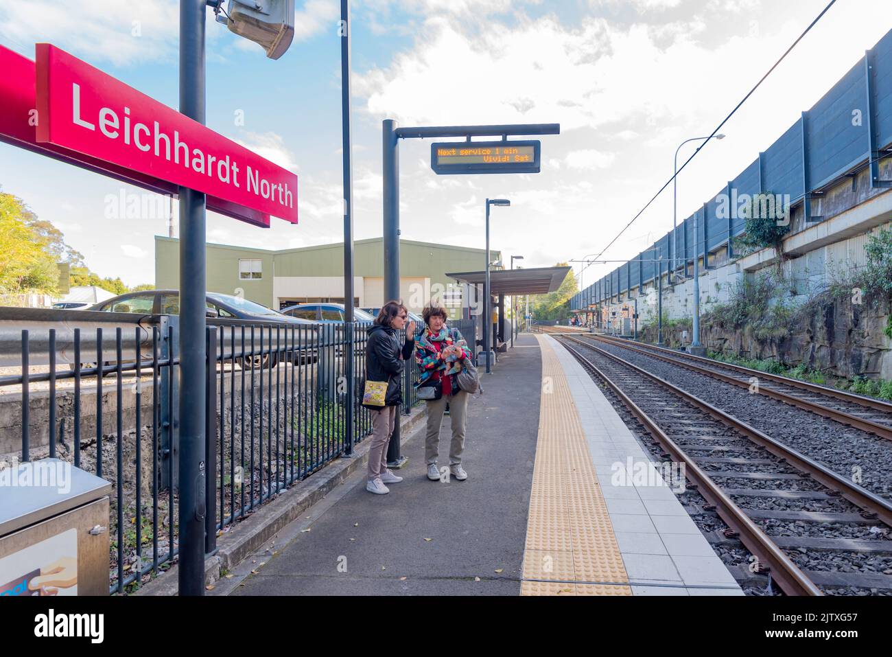 Zwei Frauen stehen auf einer Bahnhofsplattform und blicken auf ein iphone in Sydney, Australien. Straßenbahnhaltestelle Leichhardt North Stockfoto