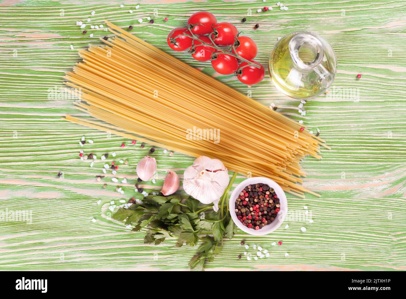 Pasta und Gargut auf grüner Holzoberfläche. Spaghetti, Tomaten, Olivenöl, Gewürzen, Knoblauch und Petersilie. Italienisches Küchenkonzept. Draufsicht, FLA Stockfoto