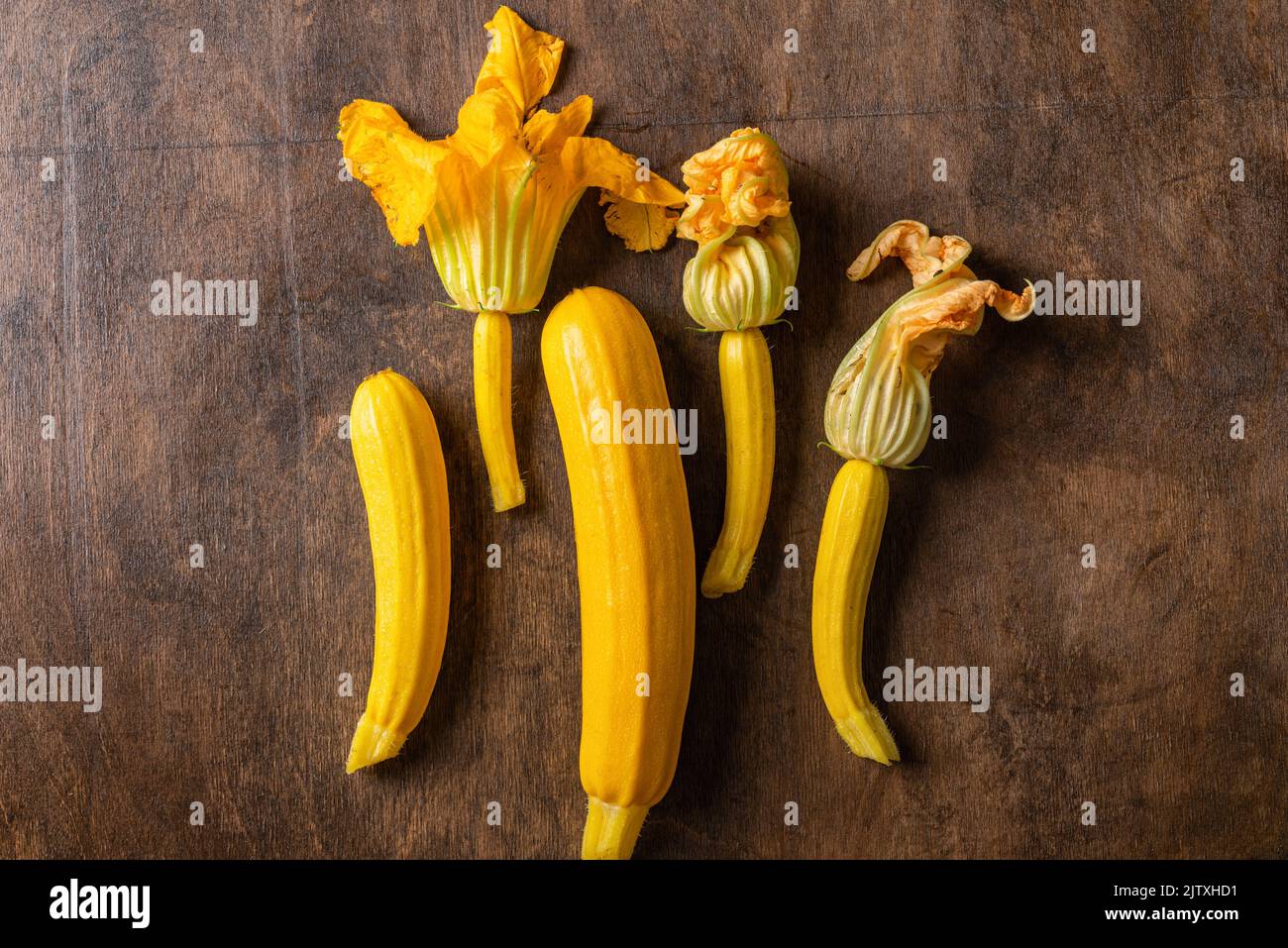 Frische gelbe Zucchini oder Squash mit Blumen auf Holzgrund. Draufsicht. Vegane Bio-Lebensmittel. Frisch geerntetes Gemüse. Stockfoto