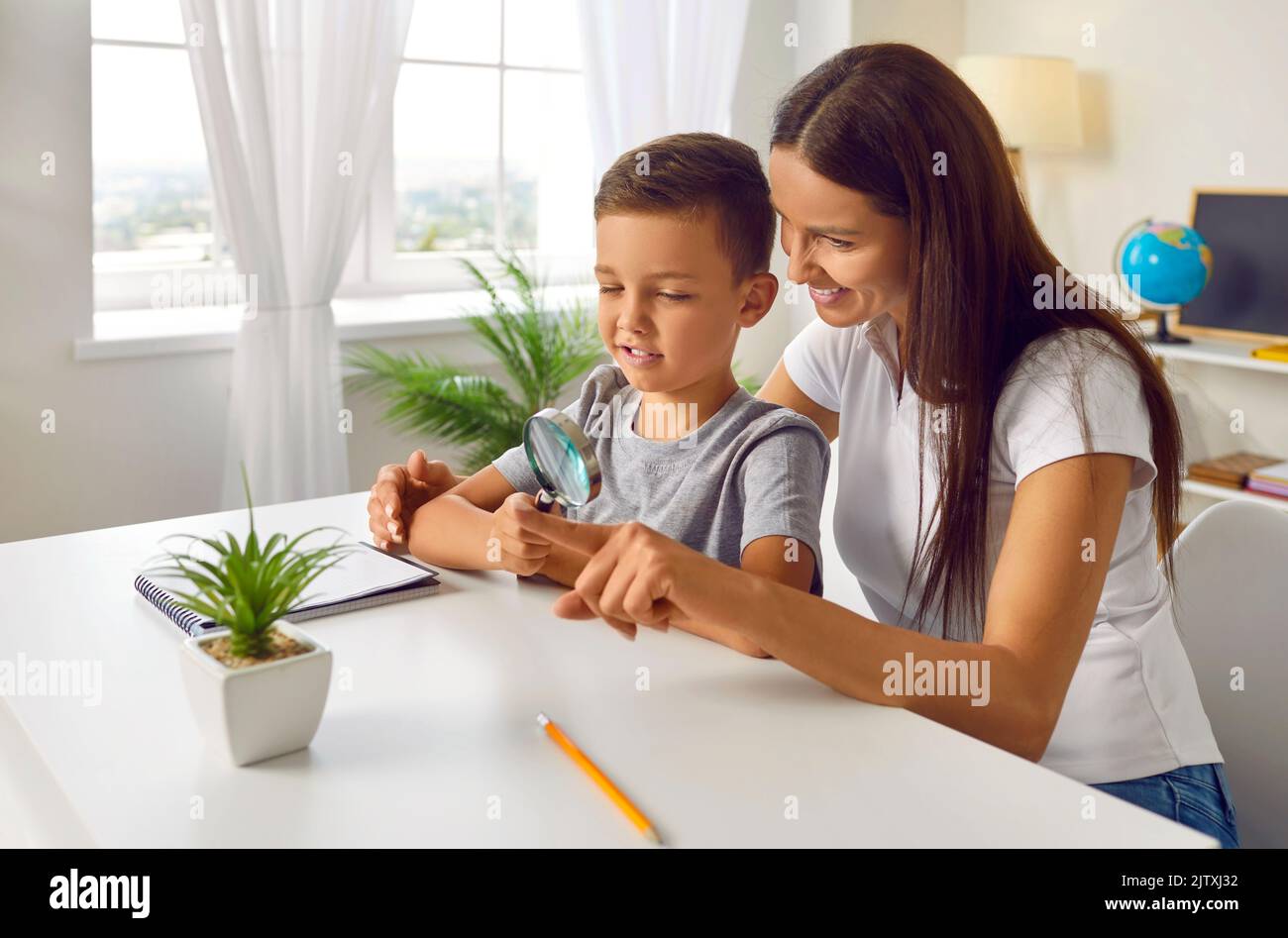 Glücklicher Schuljunge zusammen mit Mutter oder Lehrer mit Lupe während des Unterrichts Stockfoto