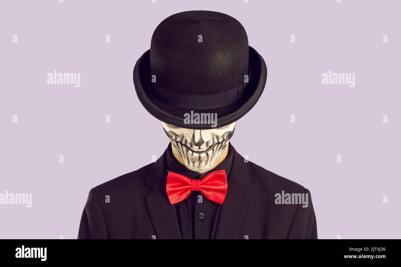 Skelett Mann in schwarzem Anzug und roter Fliege versteckt sein Halloween Totenkopf Gesicht unter schwarzem Hut Stockfoto