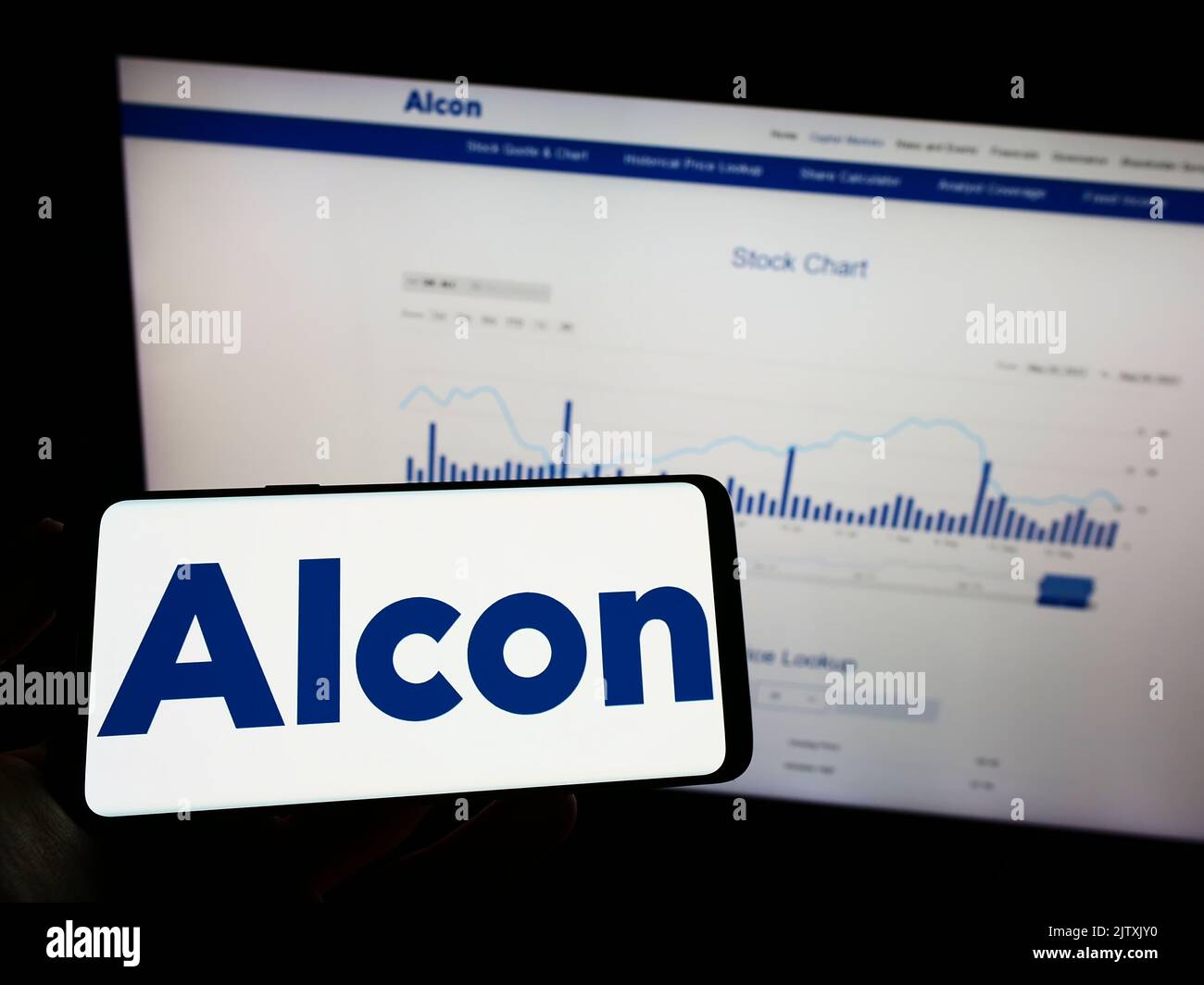 Person mit Mobiltelefon und Logo des Augenpflegeunternehmens Alcon AG auf dem Bildschirm vor der Business-Webseite. Konzentrieren Sie sich auf die Telefonanzeige. Stockfoto