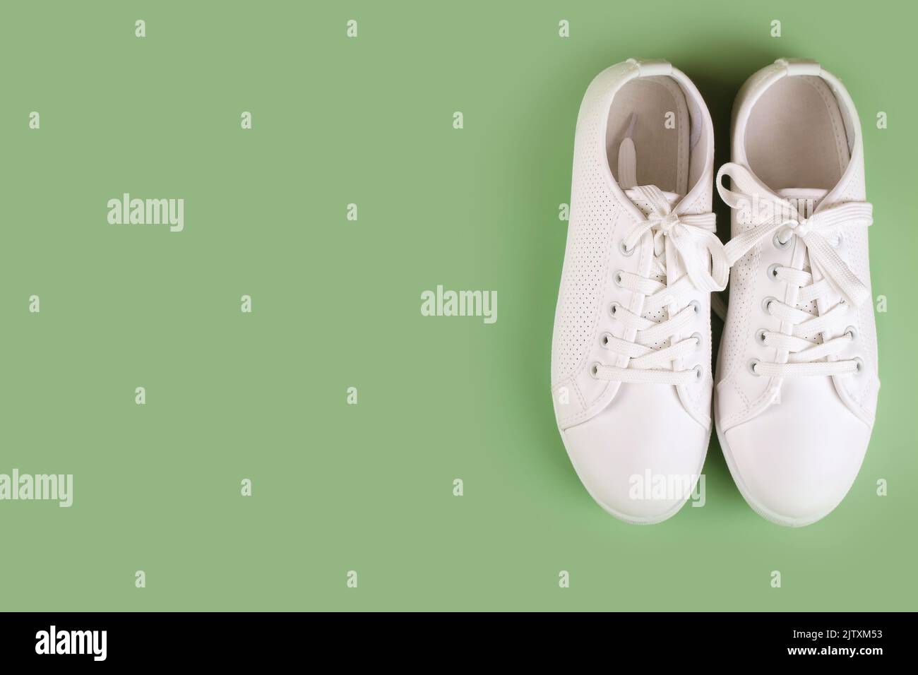 Weiße weibliche Sneakers auf grünem Hintergrund mit Kopierraum. Draufsicht, flach liegend. Mode-Mockup Stockfoto
