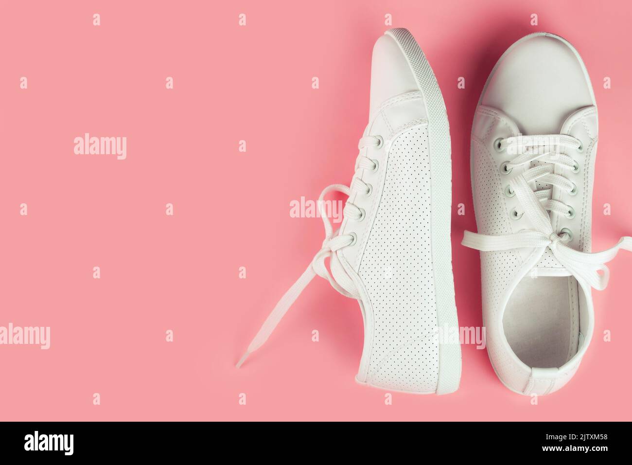 Weiße weibliche Sneakers auf rosa Hintergrund mit Kopierraum. Draufsicht, flach liegend. Stockfoto