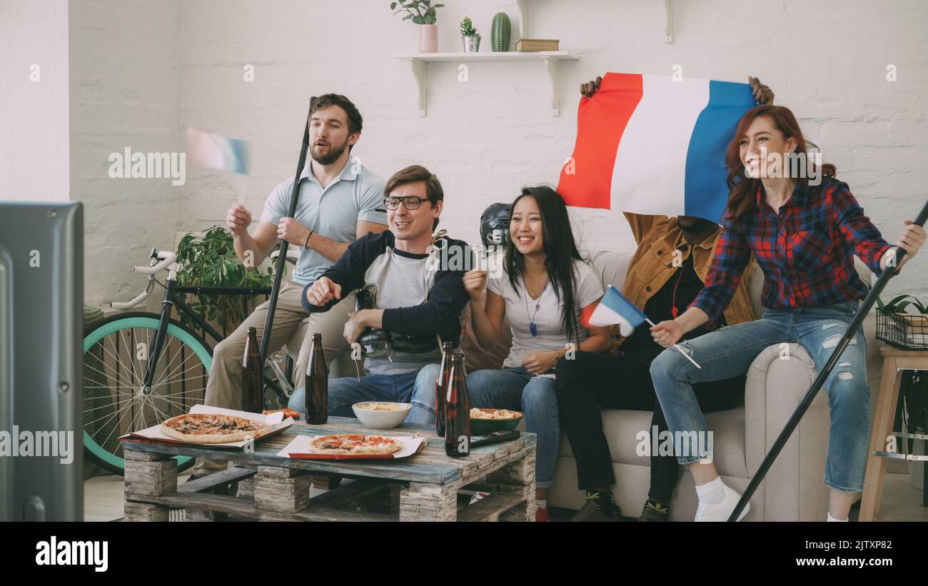 Gruppe junger Freunde Sportfans mit französischen Nationalflaggen, die im Fernsehen die Sportmeisterschaft verfolgen, jubeln gemeinsam die Lieblingsmannschaft zu Hause an Stockfoto