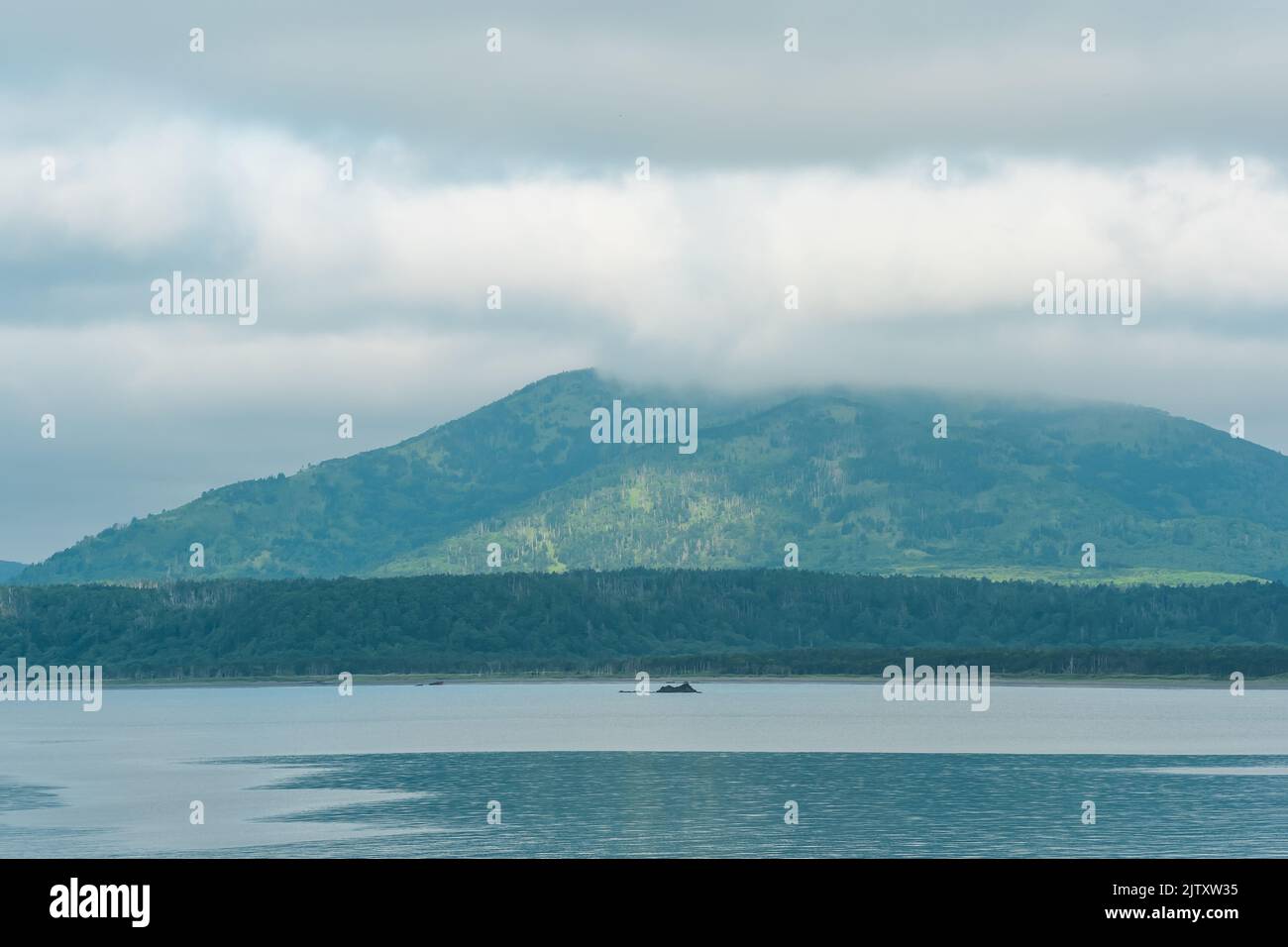 Meeresbucht mit nebligen Bergen im Hintergrund, Blick auf den Mendelejew-Vulkan an einem bewölkten Tag Stockfoto