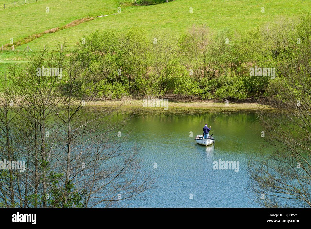 Ein Mann, der im Frühjahr von einem Boak auf dem Clatworthy Reservoir an den Südhängen der Brendon Hills, Somerset, England, fischt. Stockfoto