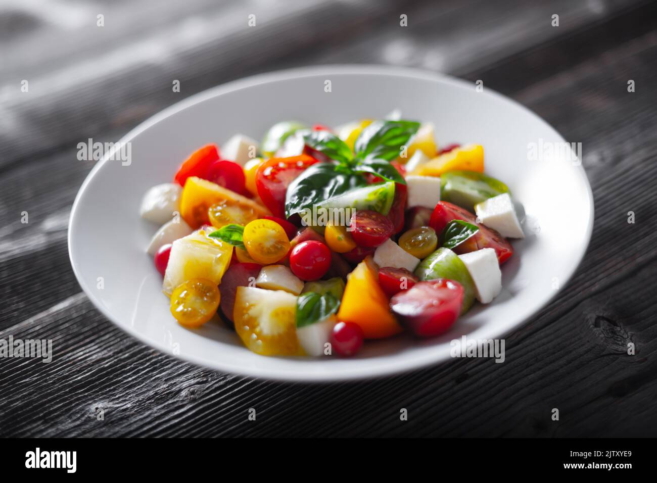 Salat mit verschiedenen Sorten, rote, gelbe, grüne und schwarze Tomatenmischung, Mozzarella-Käse und Basilikum. Caprese Salas mit frischen bunten Tomaten. Food-Fotografie Stockfoto