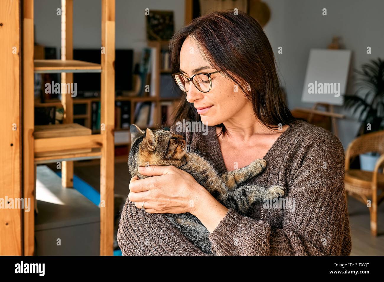 Frau mittleren Alters umarmt niedliche tabby Katze in Indoor-Szene. Mensch-Tier-Beziehungen. Lustige Heimtiere. Heimatlose Haustiere. Stockfoto