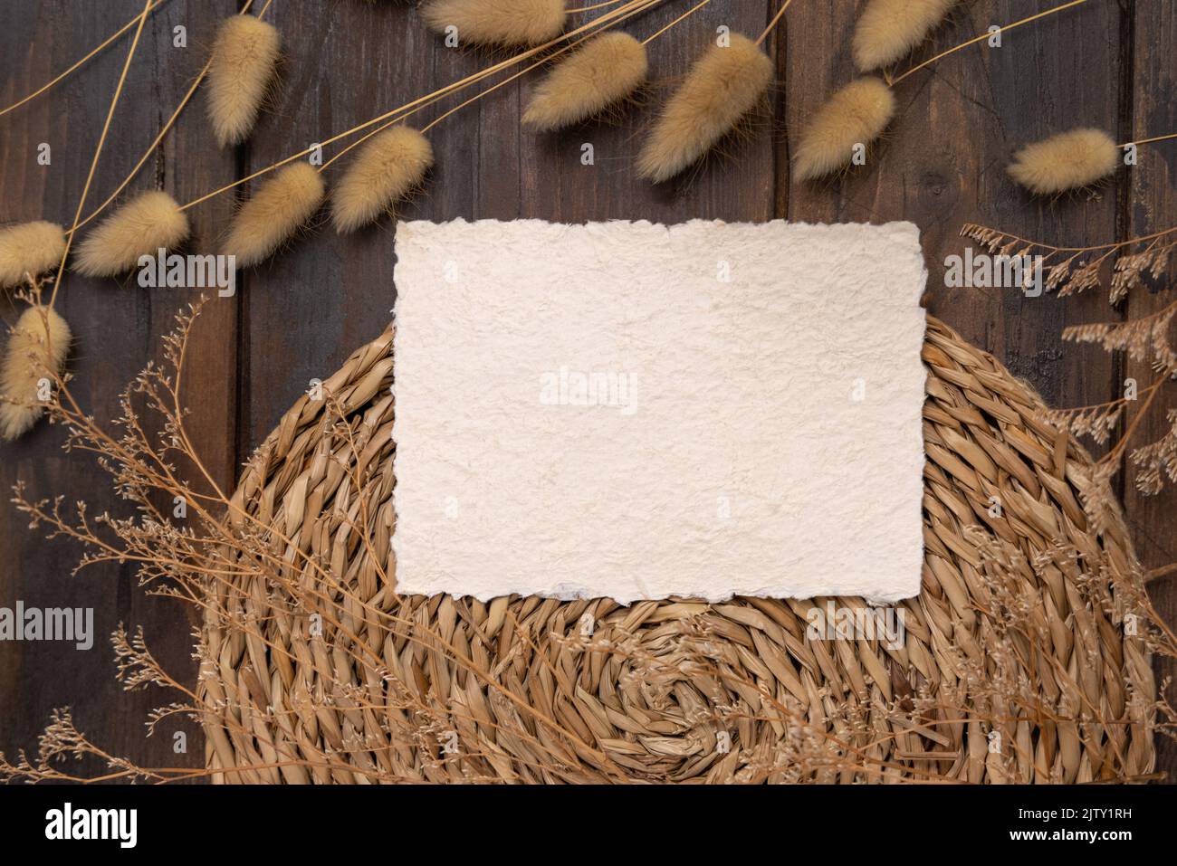 Leere Karte und Umschlag auf geklapptem Tischset auf Holz in der Nähe von Hare's Tail Grass Draufsicht. Boho-Szene mit horizontaler Papierkarte. Böhmisch oder in der Nähe der Natur Stockfoto