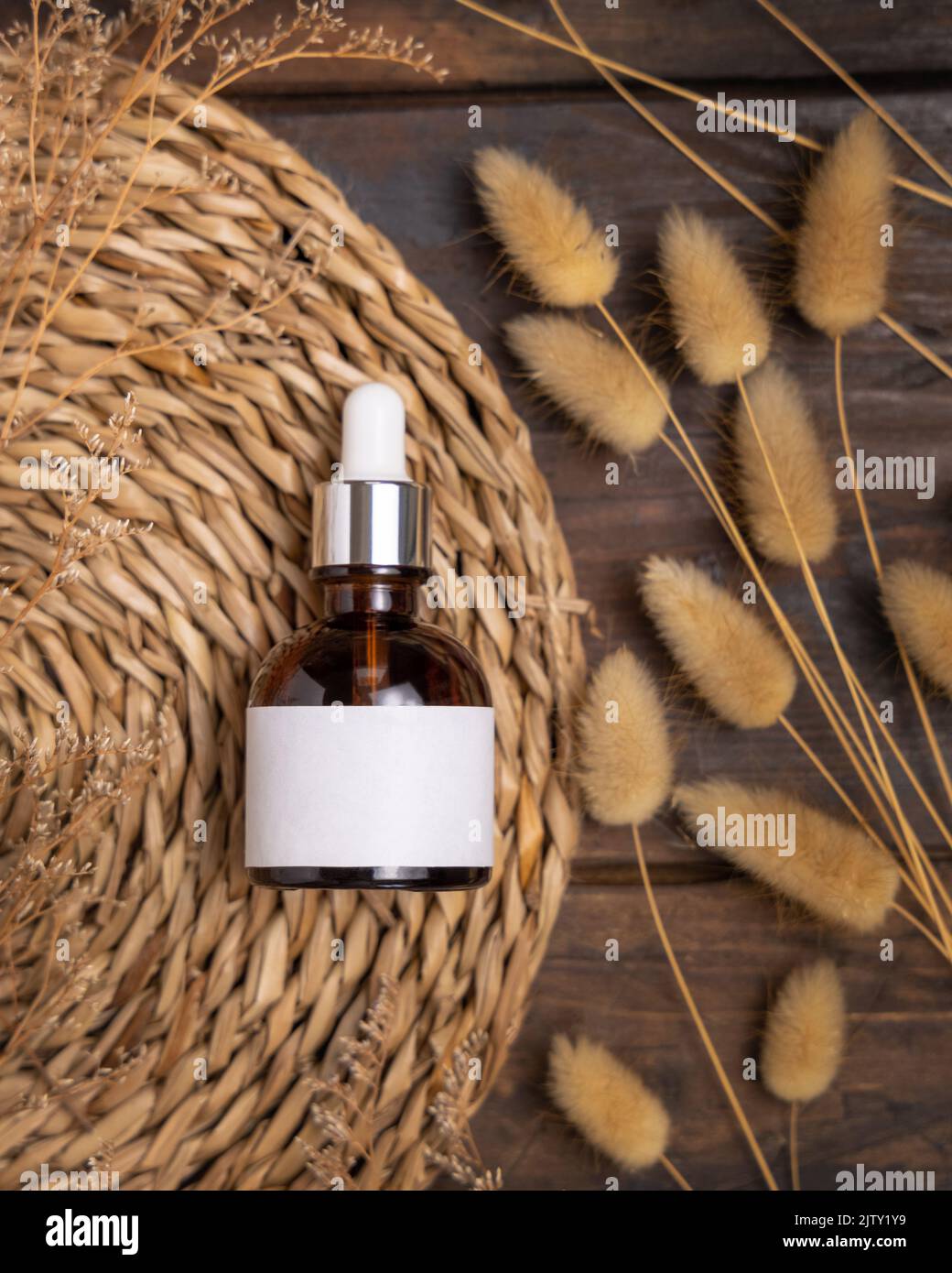 Tropfflasche aus Glas auf geklapptem Tischset in der Nähe von Hare's Tail Grass, Draufsicht auf Holz, Etikett Mockup. Natürliches Hautpflegeprodukt, Serum oder Essenz. Böhmische e Stockfoto