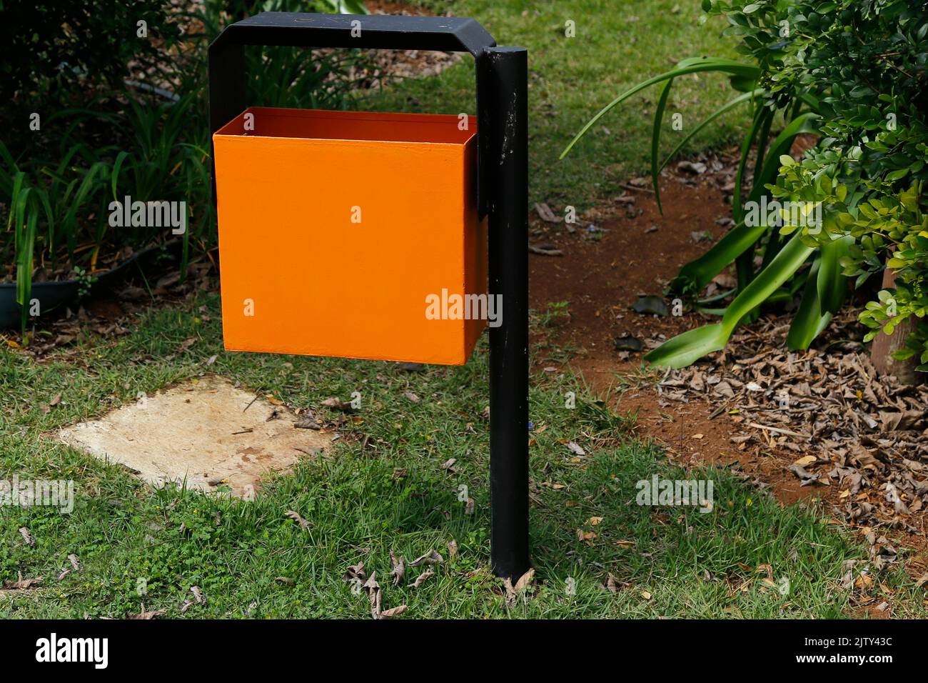 Orangefarbener Metallabfallbehälter im grünen und begrünten öffentlichen Bereich - Müllabfuhr Stockfoto