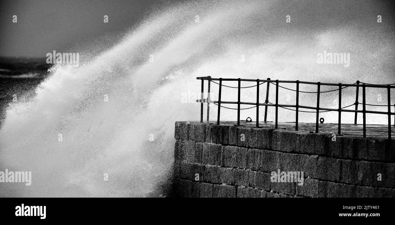 Große Wellen schlagen in und über dem Porthleven Pier. Stockfoto