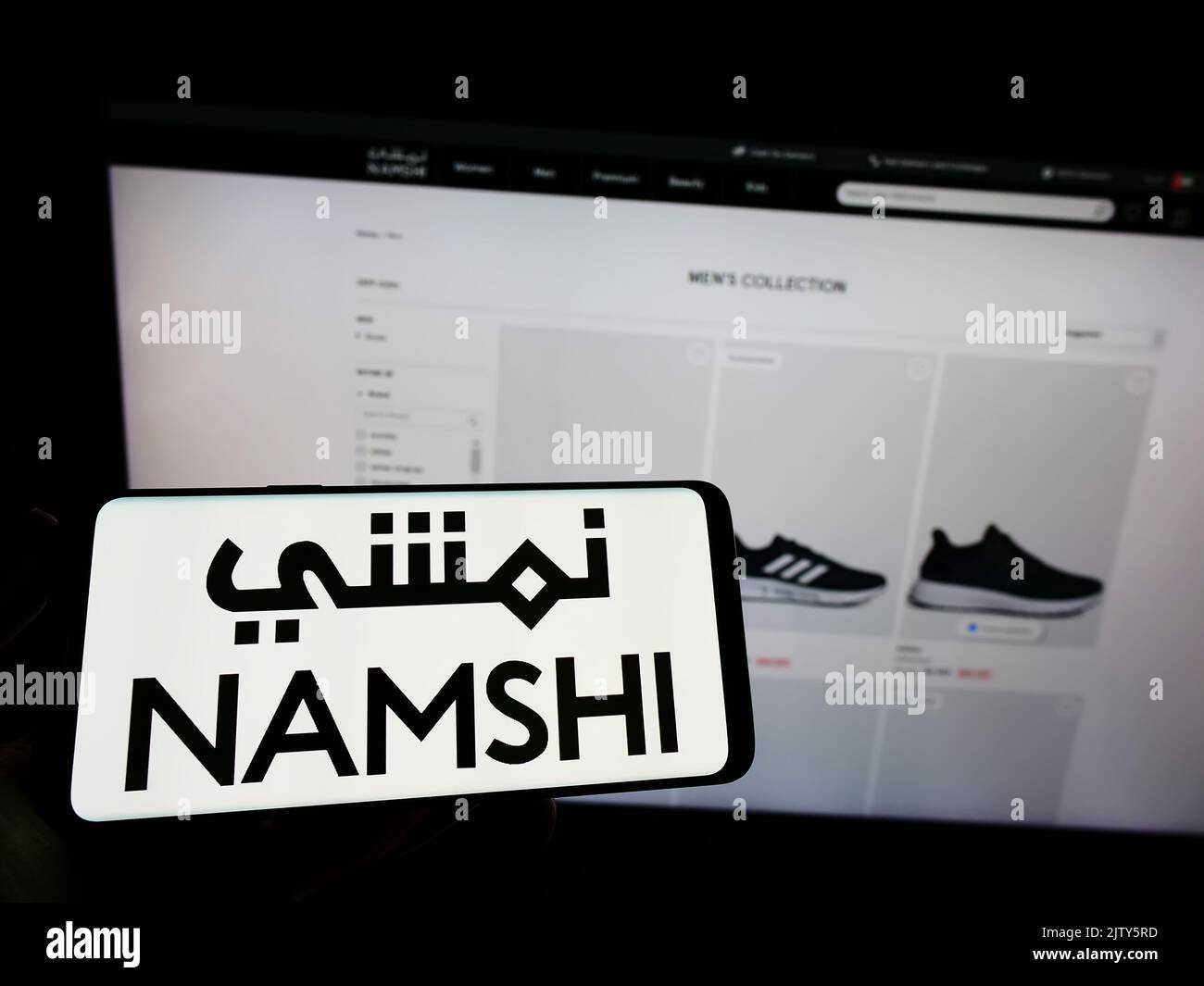 Person, die Mobiltelefon mit dem Logo des arabischen E-Commerce-Unternehmens Namshi auf dem Bildschirm vor der Business-Webseite hält. Konzentrieren Sie sich auf die Telefonanzeige. Stockfoto