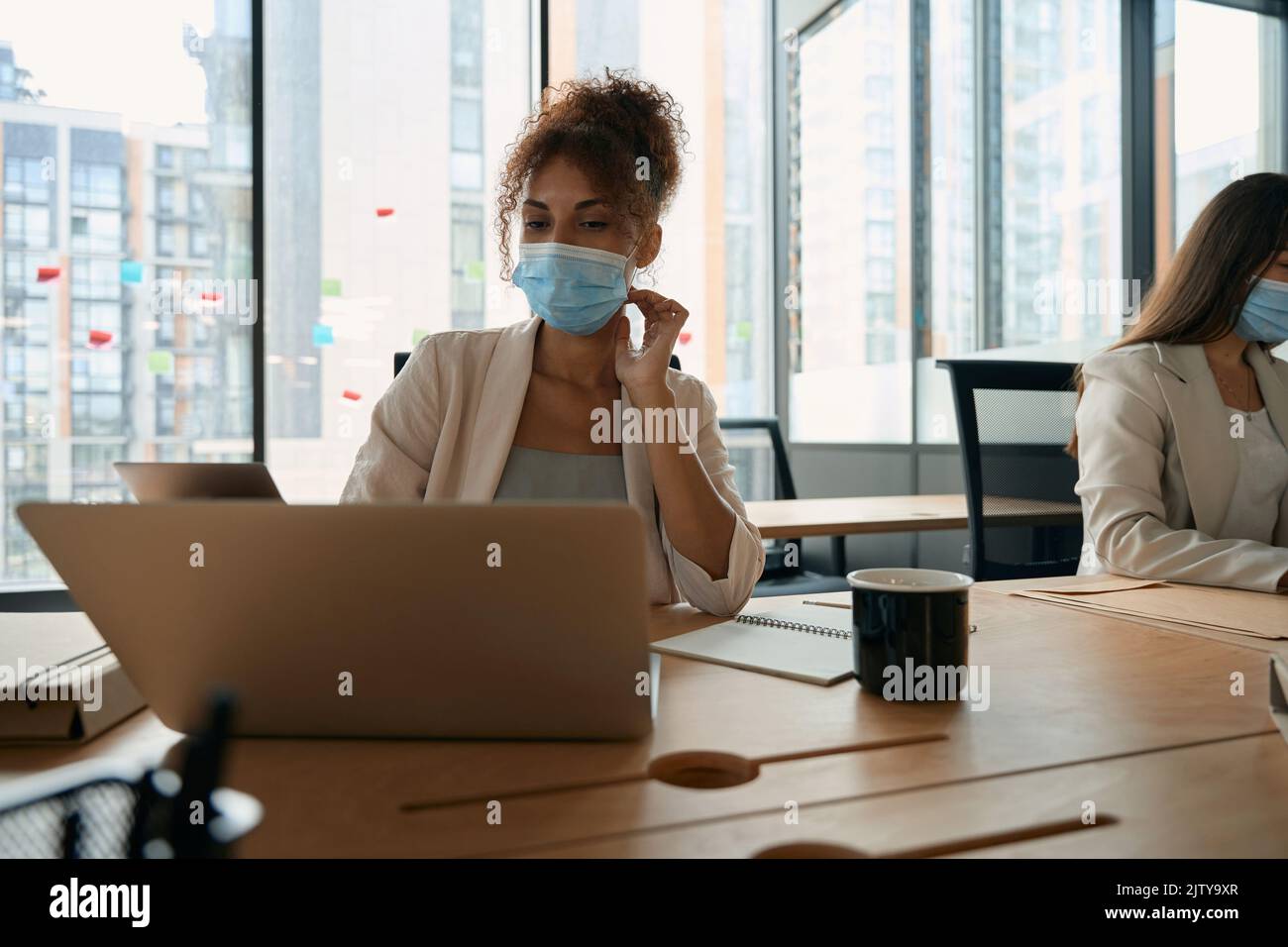 Geschäftsfrauen in Schutzmasken arbeiten im Büro mit Fenstern Stockfoto