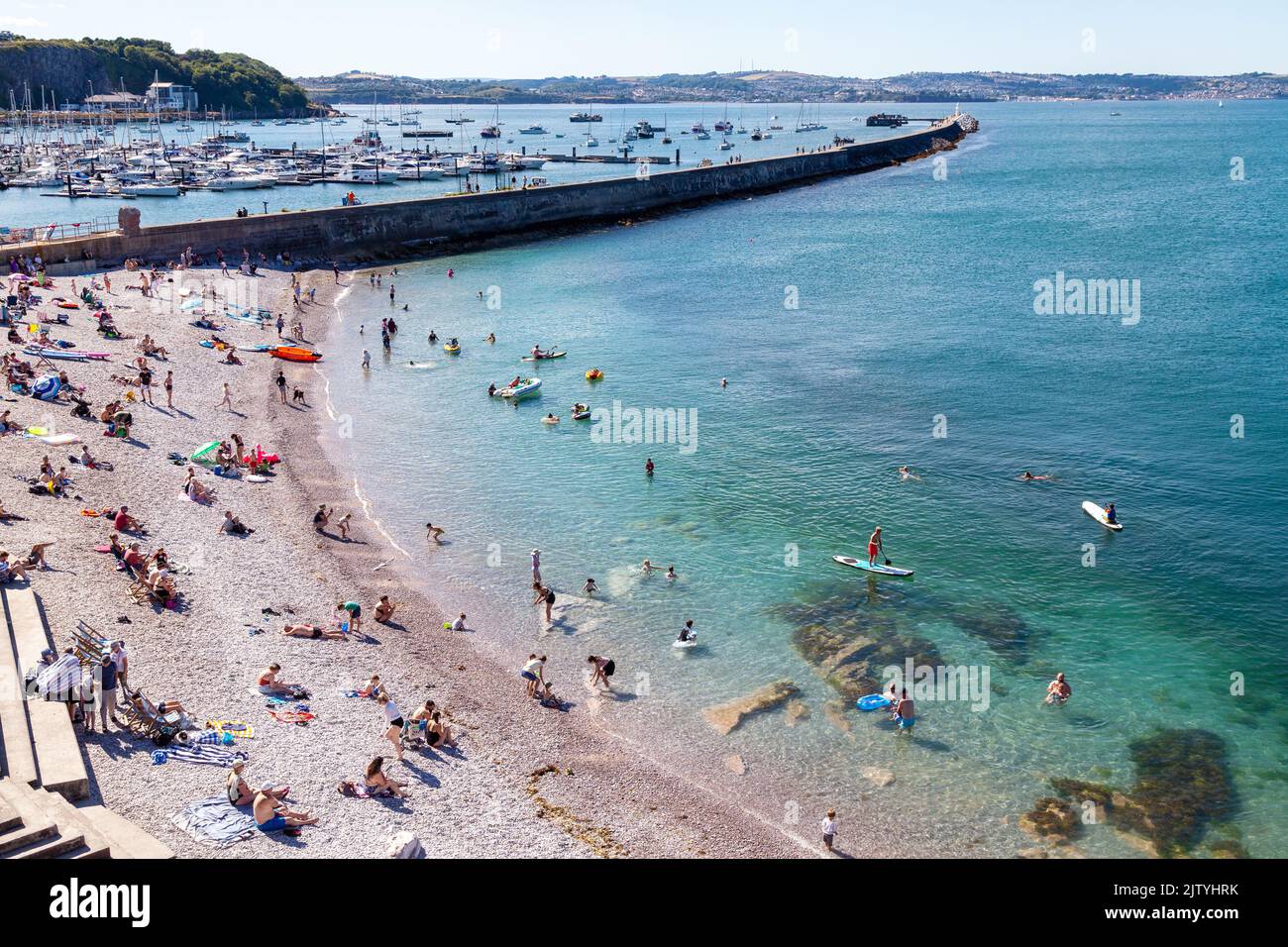 Ein belebtes Brixham Beach mit dem Wellenbrecher im Hintergrund. Stockfoto