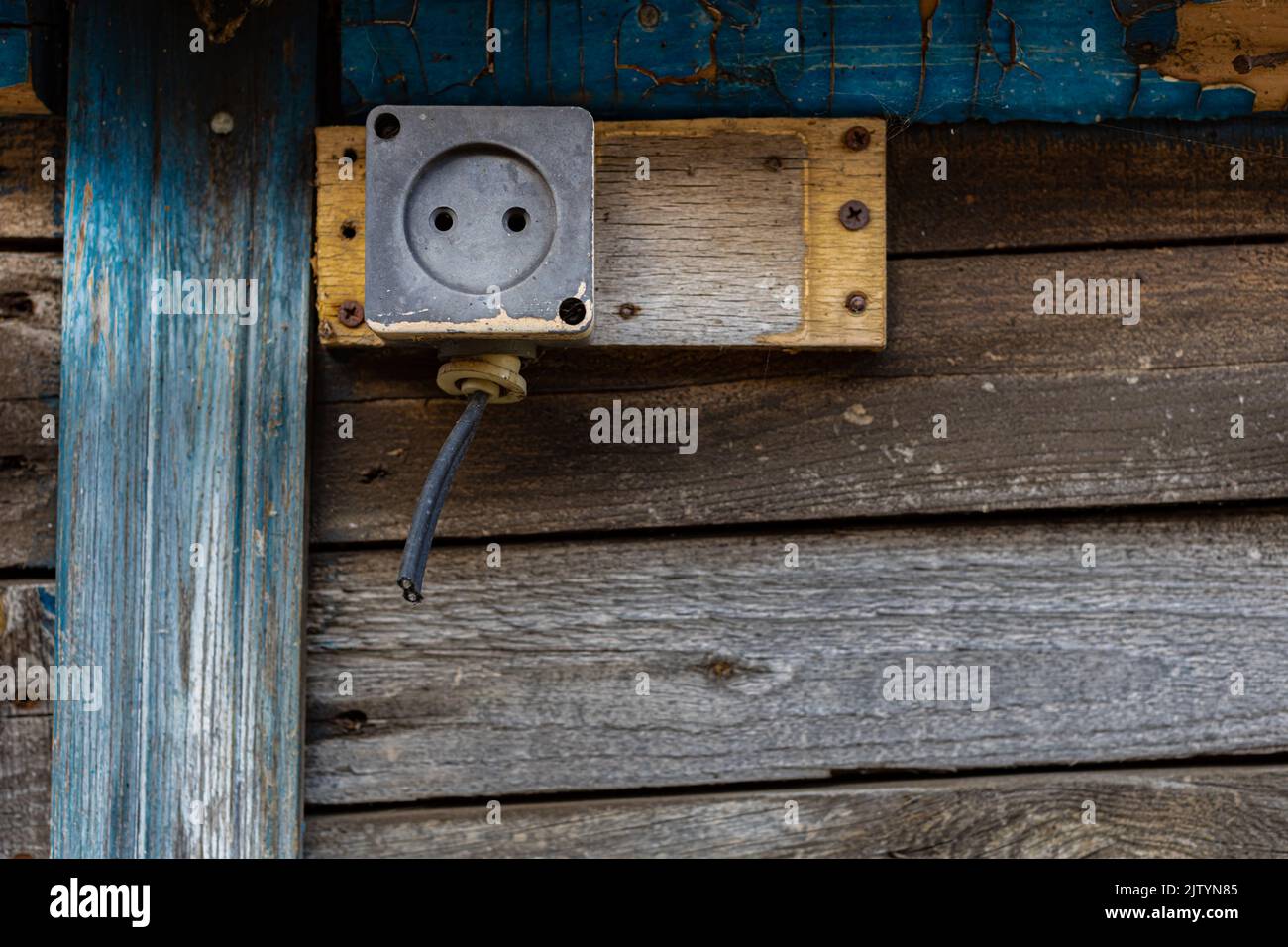 Eine alte Steckdose mit einem abgeschnittenen Draht, der an ein Holzgebäude genagelt wurde Stockfoto