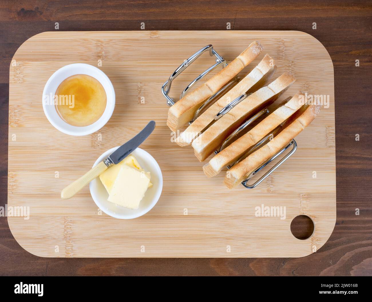 Flacher Toastständer, gefüllt mit Toastbuttermesser und Marmelade auf einem Holzhintergrund Stockfoto