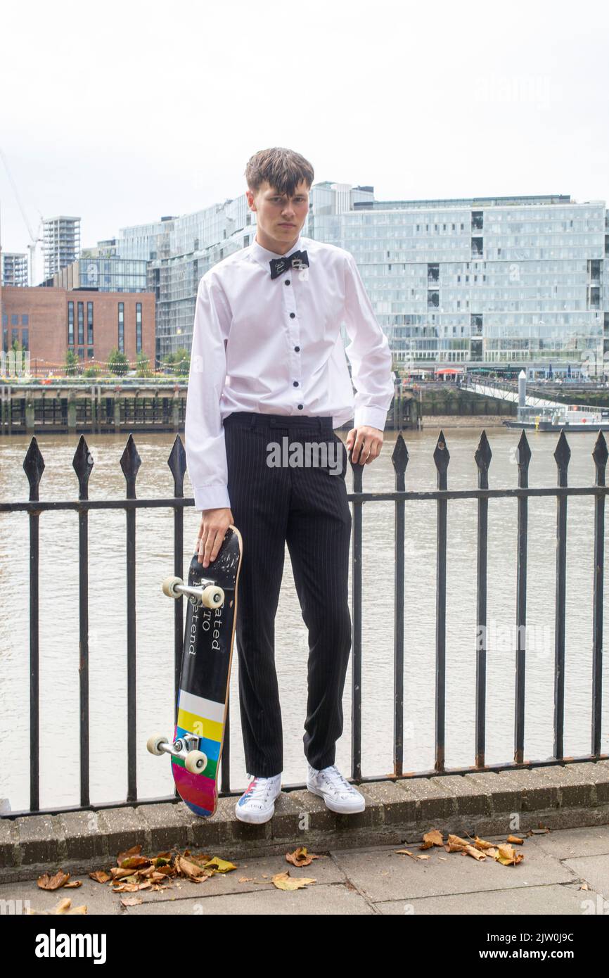 Hübscher Millennial-Mann mit Fliege, der sein Skateboard hält Stockfoto