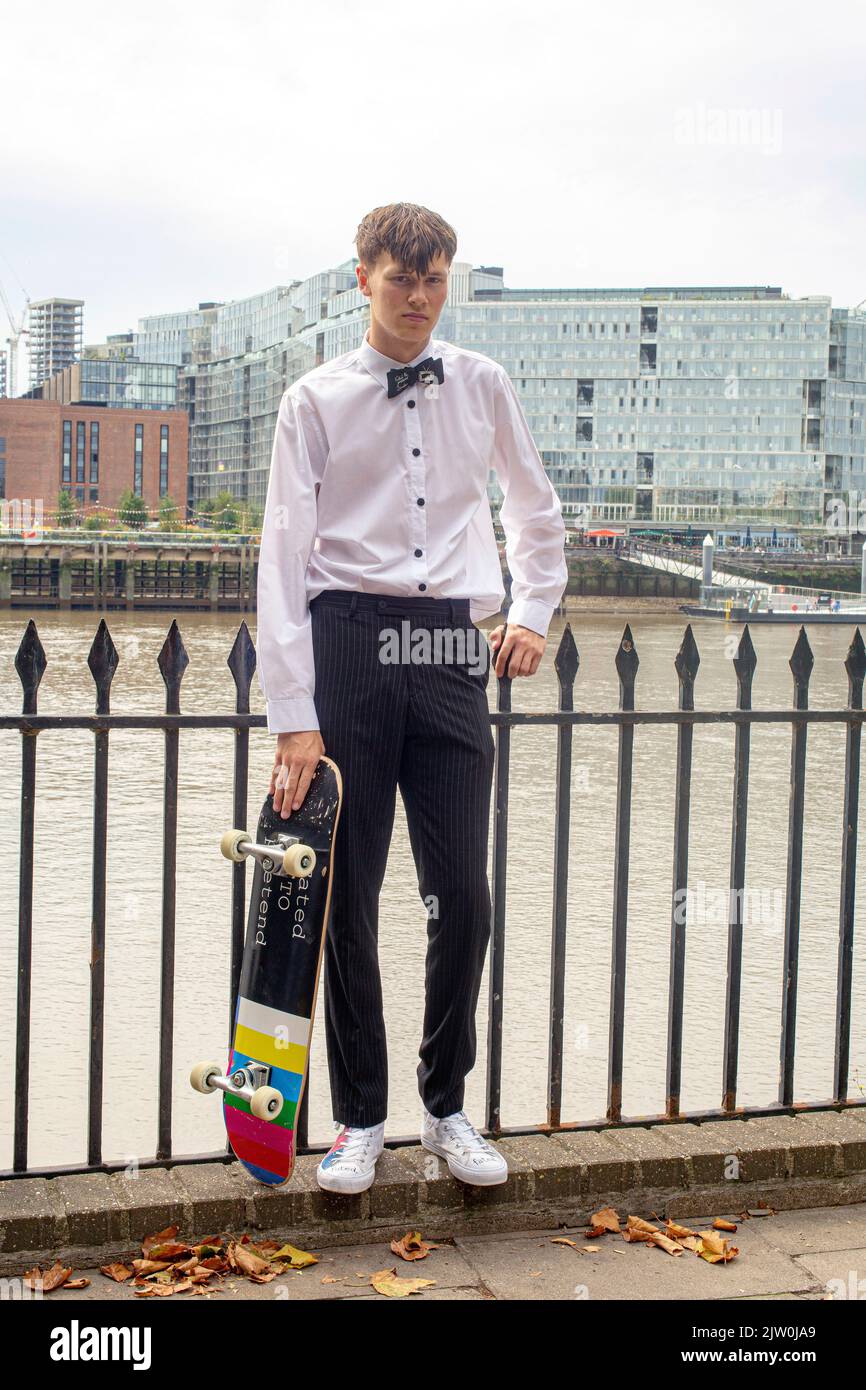 Hübscher Millennial-Mann mit Fliege, der sein Skateboard hält Stockfoto