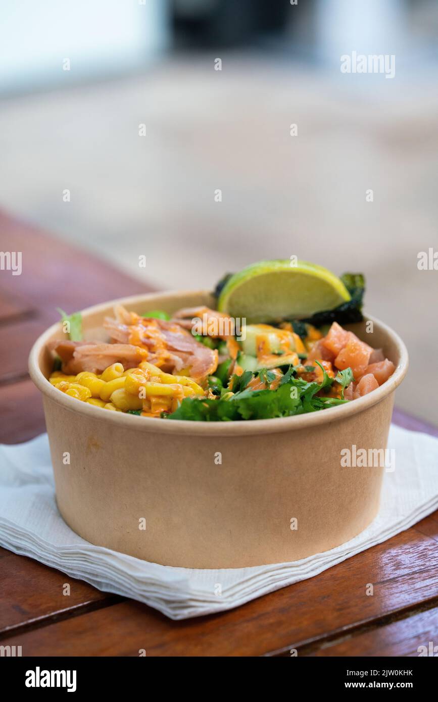 Eine vertikale Aufnahme einer Papierschüssel mit köstlichem Poke mit Mais, Lachs, Algen, Limette und würzigem Mayo Stockfoto