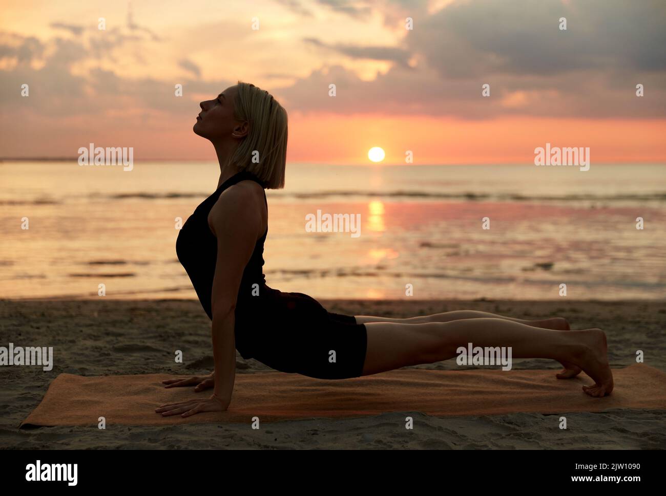 Frau, die Yoga nach oben macht, stellt sich mit Hund am Strand auf Stockfoto