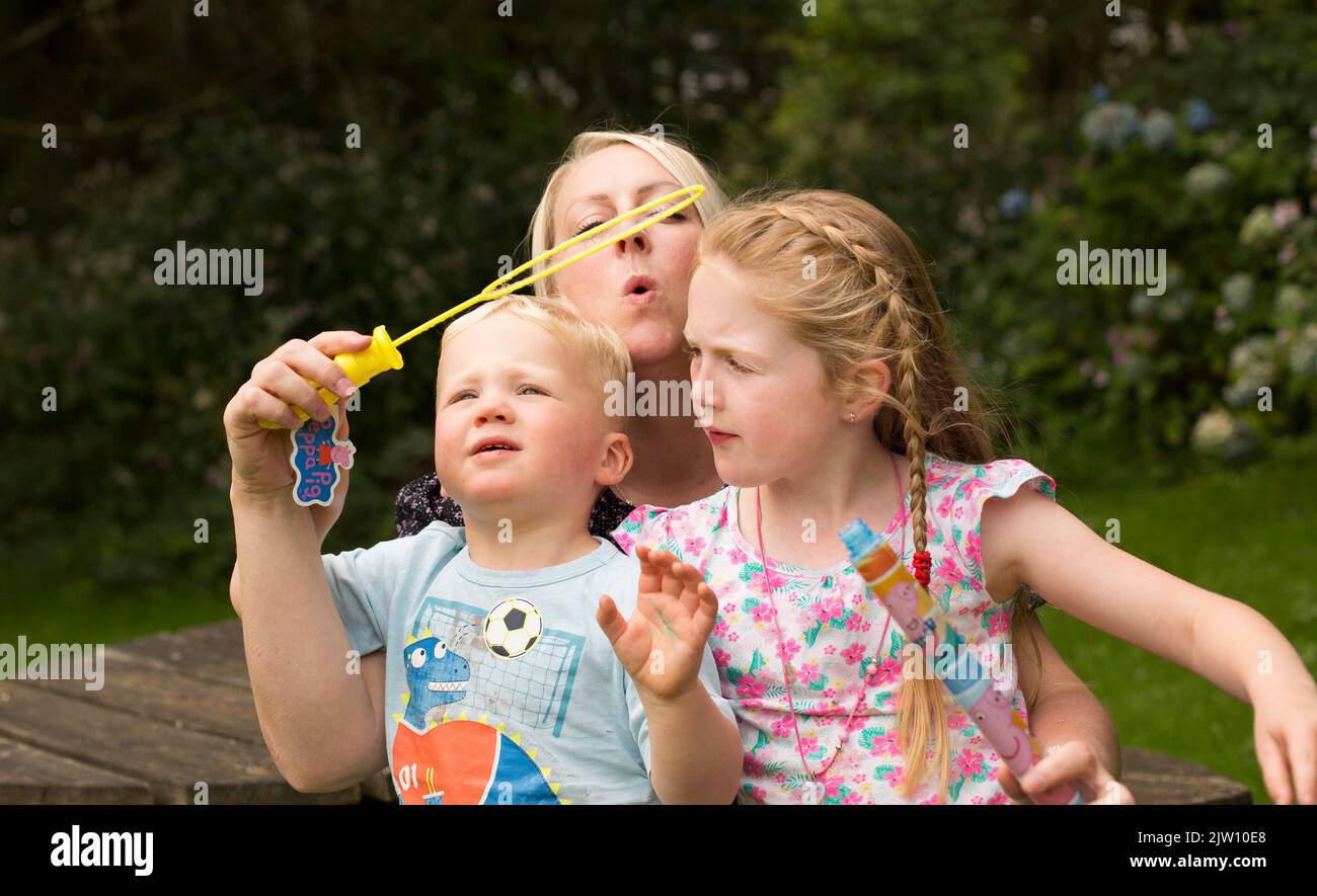 Mutter bläst Blasen mit ihren 2 Kindern Stockfoto