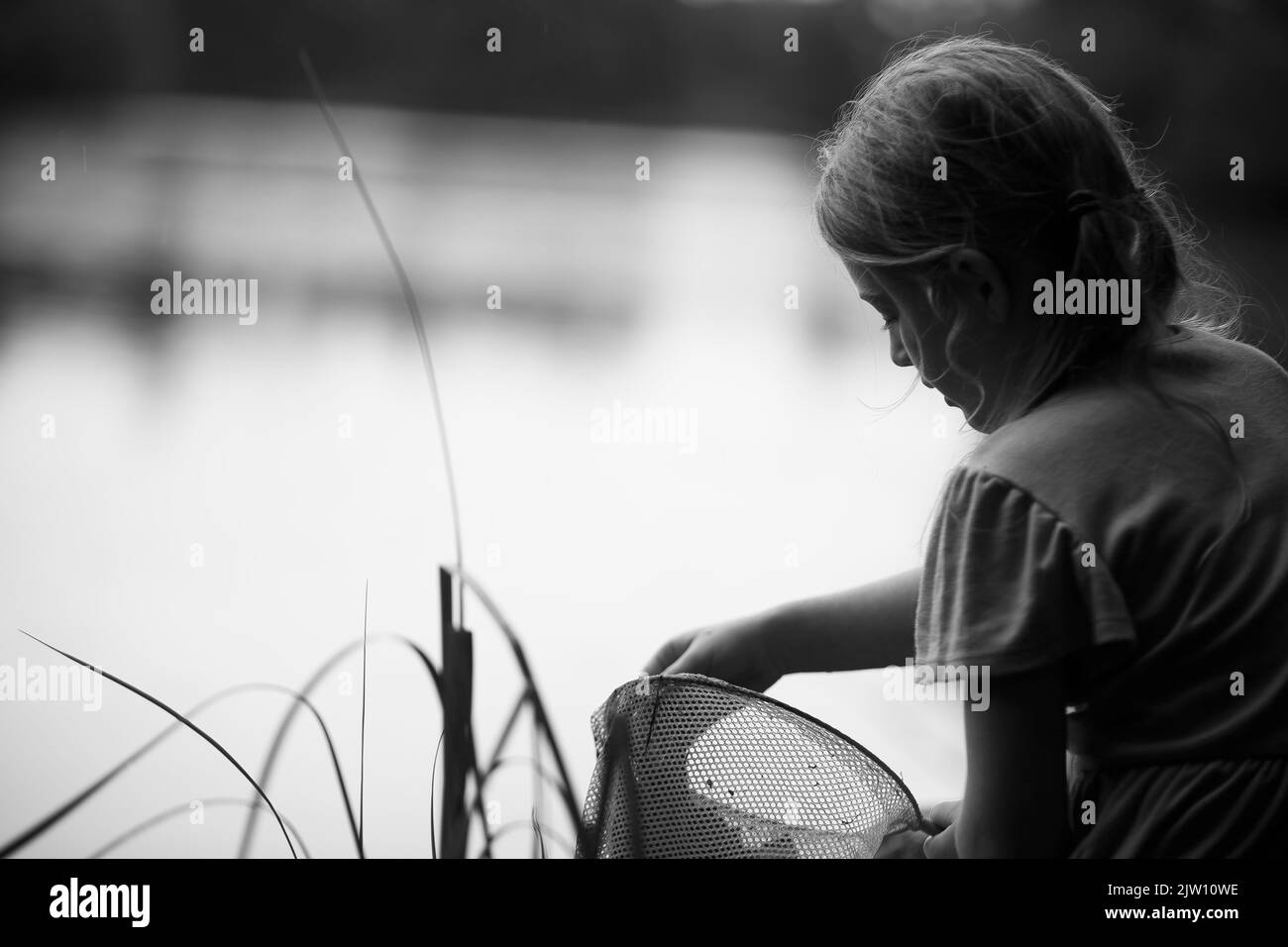 Das junge kaukasische Mädchen sitzt an einem See und erkundet, was sie in ihrem Netz hat. Stockfoto