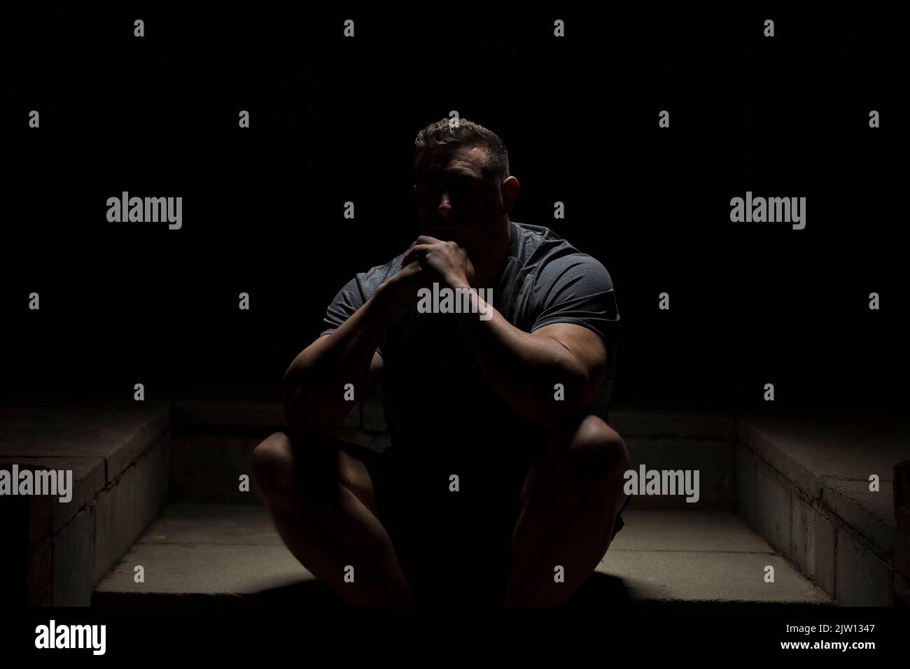 Ein Männchen sitzt auf einem Schritt in der Dunkelheit und schaut in die Kamera. Stockfoto