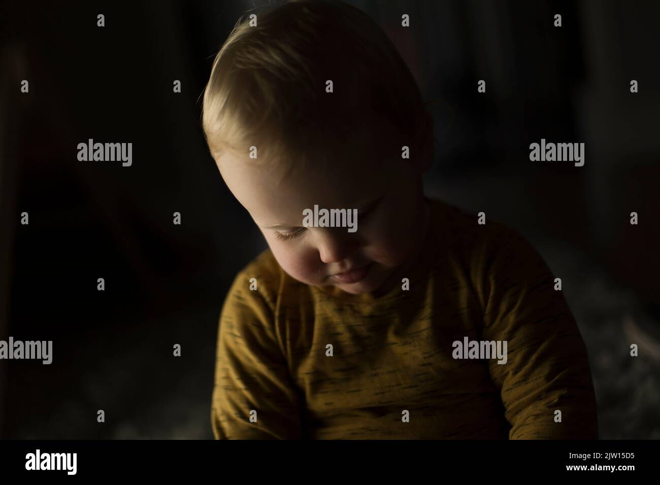 Junges Kleinkind, das in einem dunklen Raum nach unten schaut, Studiolicht verwendet. Stockfoto