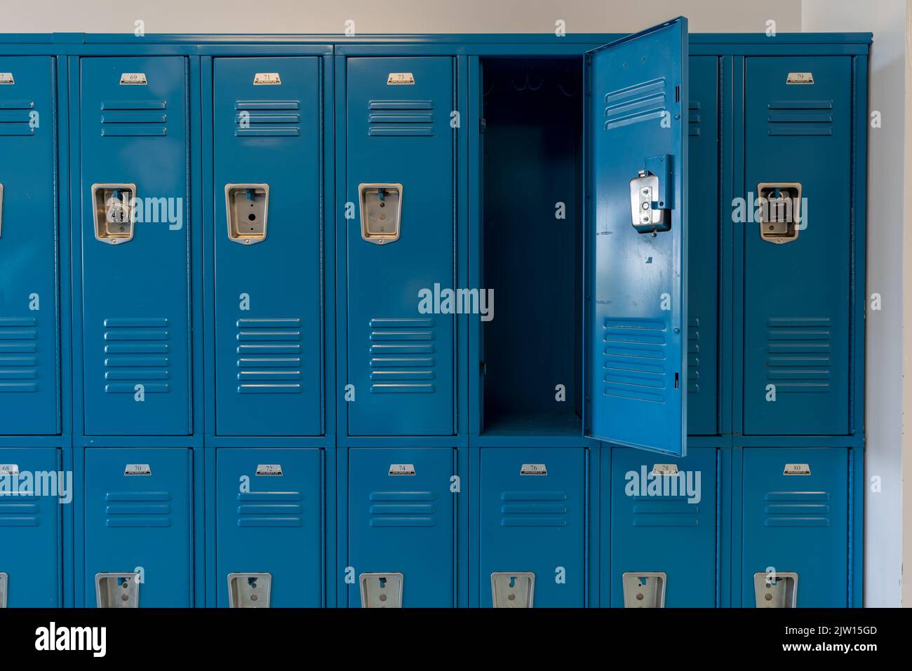 Schließfächer aus blauem Metall entlang eines unscheinbaren Flurs in einer typischen US High School. Keine identifizierbaren Informationen enthalten und niemand in der Halle. Stockfoto