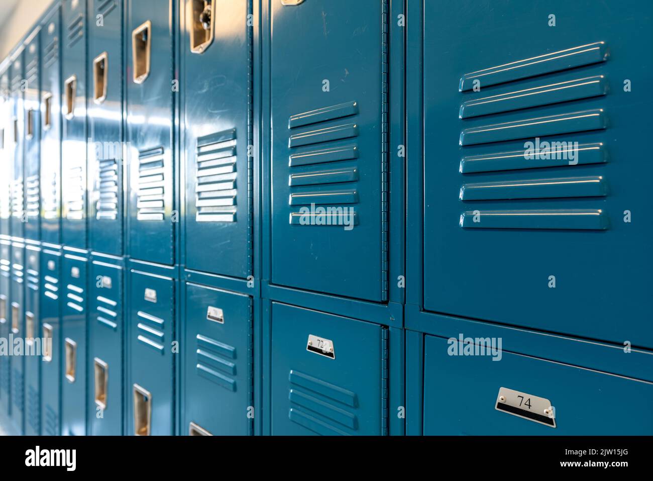 Schließfächer aus blauem Metall entlang eines unscheinbaren Flurs in einer typischen US High School. Keine identifizierbaren Informationen enthalten und niemand in der Halle. Stockfoto