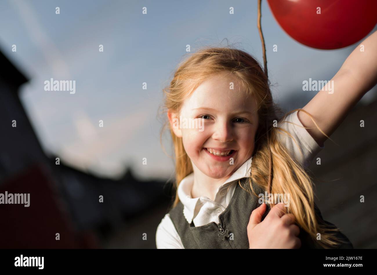 Die kaukasische junge Frau posiert mit einem großen Lächeln auf ihrem Gesicht und hält einen Stock mit angeschlossenem Ballon. Stockfoto