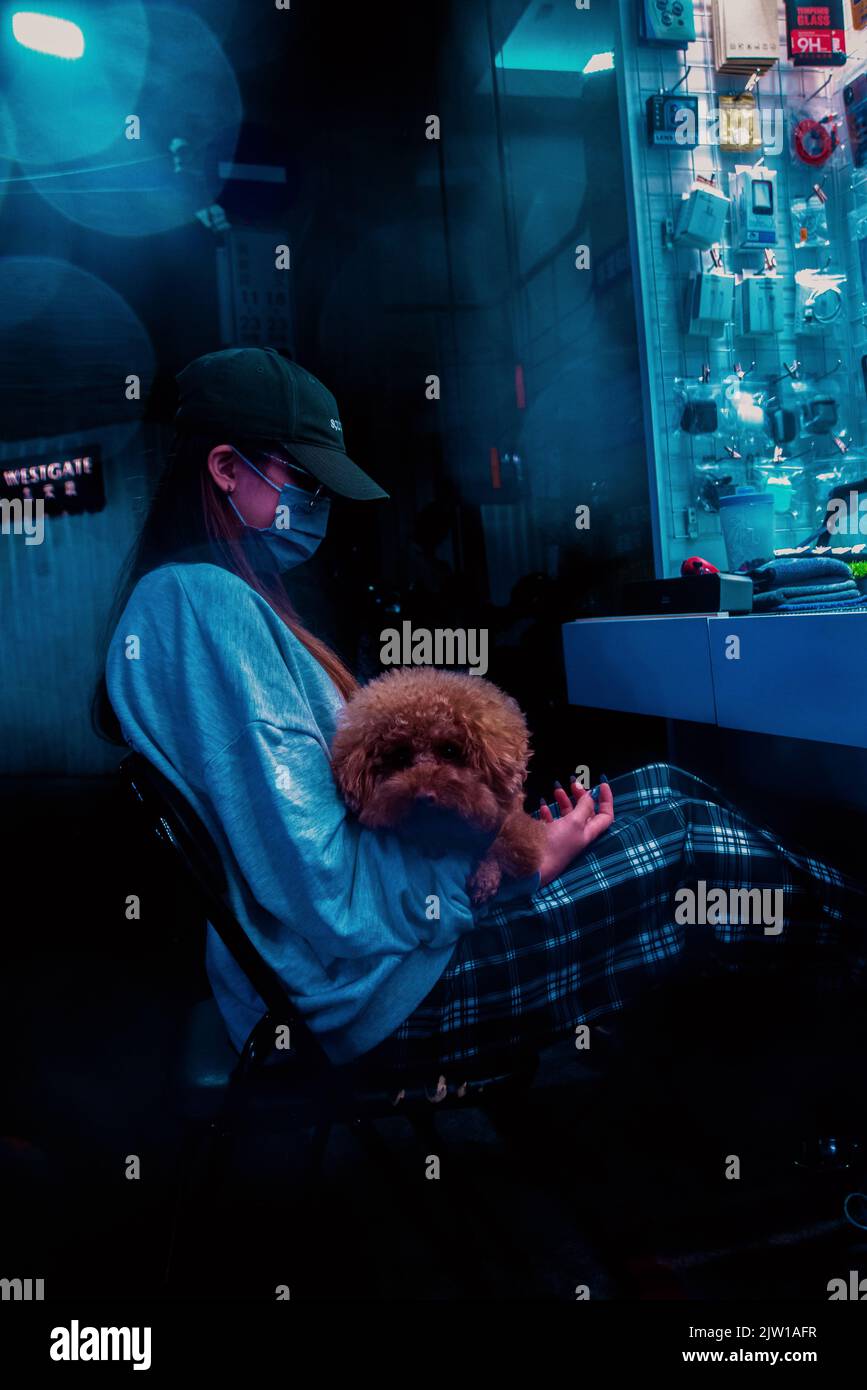 Eine vertikale Aufnahme eines Mädchens, das mit einem niedlichen Hund auf dem Schoß sitzt, mit Cyberpunk-Szenen aus dem Ximen District in Taipei, Taiwan Stockfoto