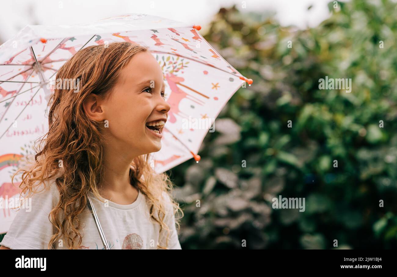 Mädchen lacht und hält einen Regenschirm draußen im Regen Stockfoto