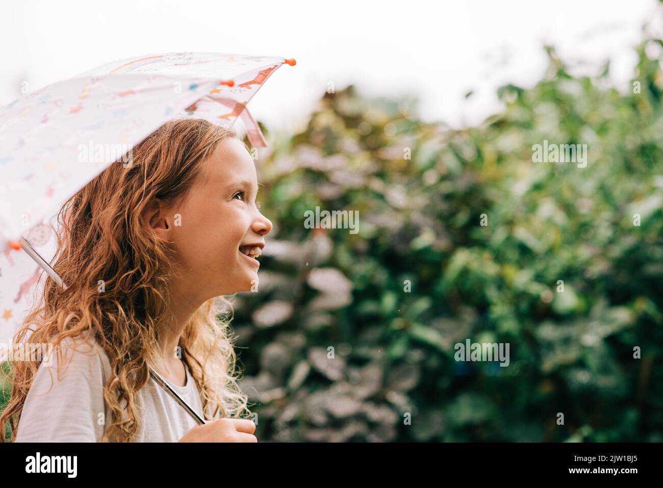 Kind lacht, während es draußen im Regen einen Regenschirm hält Stockfoto