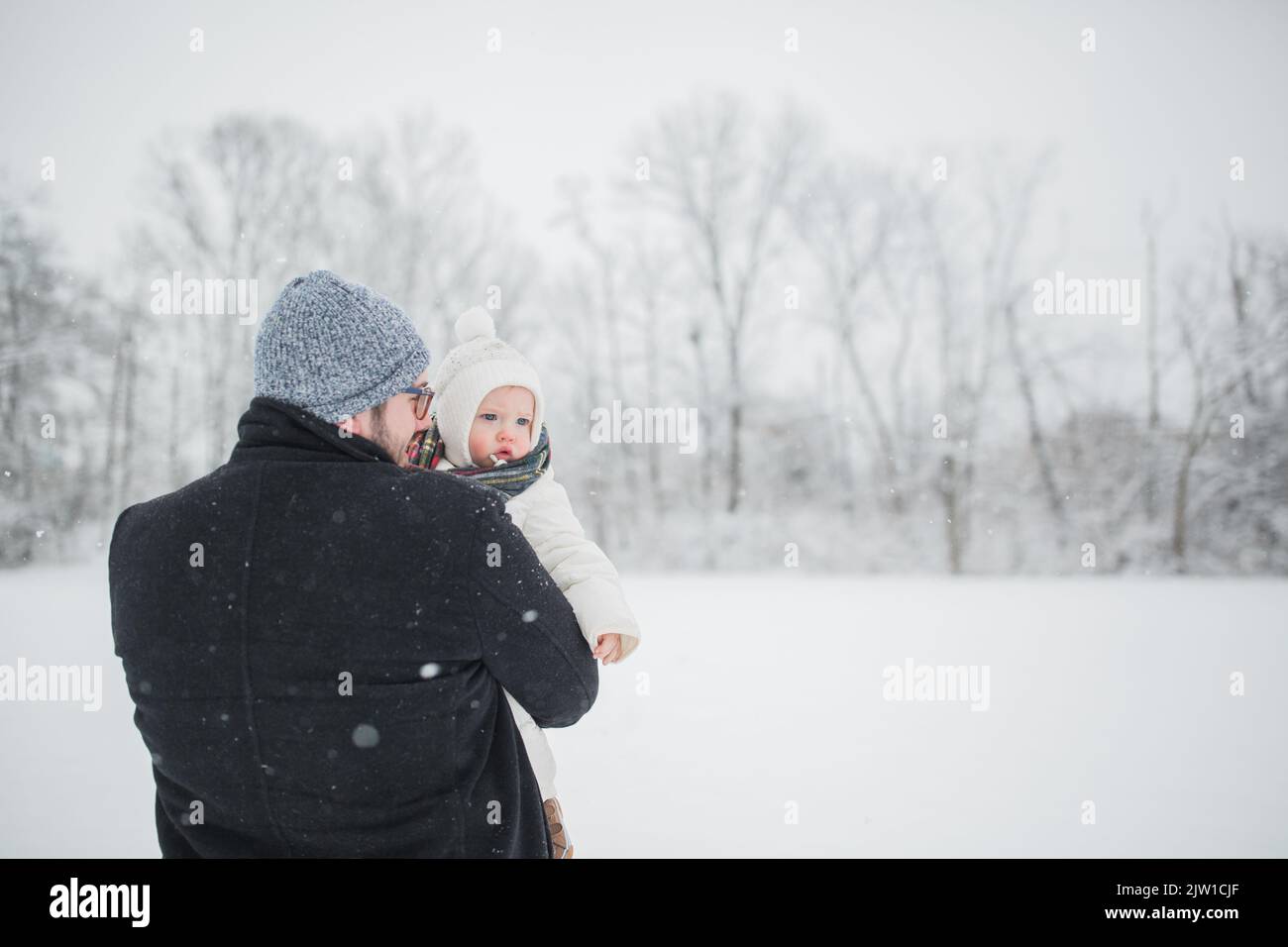 Der 30-jährige kaukasische Vater hält einen Jungen auf einem verschneiten Feld. Stockfoto