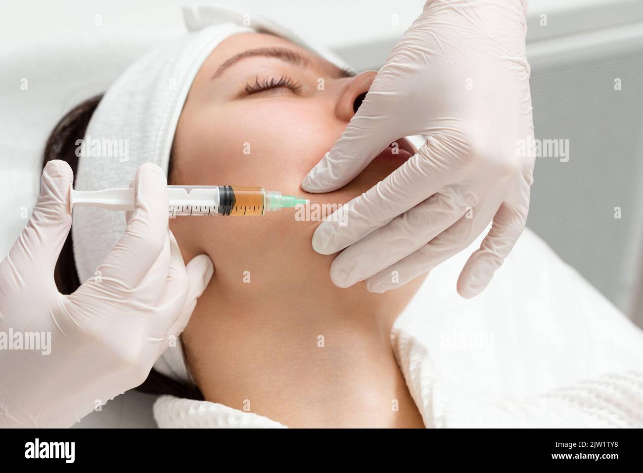 Kosmetologe gibt eine Injektion in die Wangenknochen einer jungen Frau.. Arzt injiziert Hyaluronsäure in das ching einer Frau als Gesichtsbehandlung Stockfoto