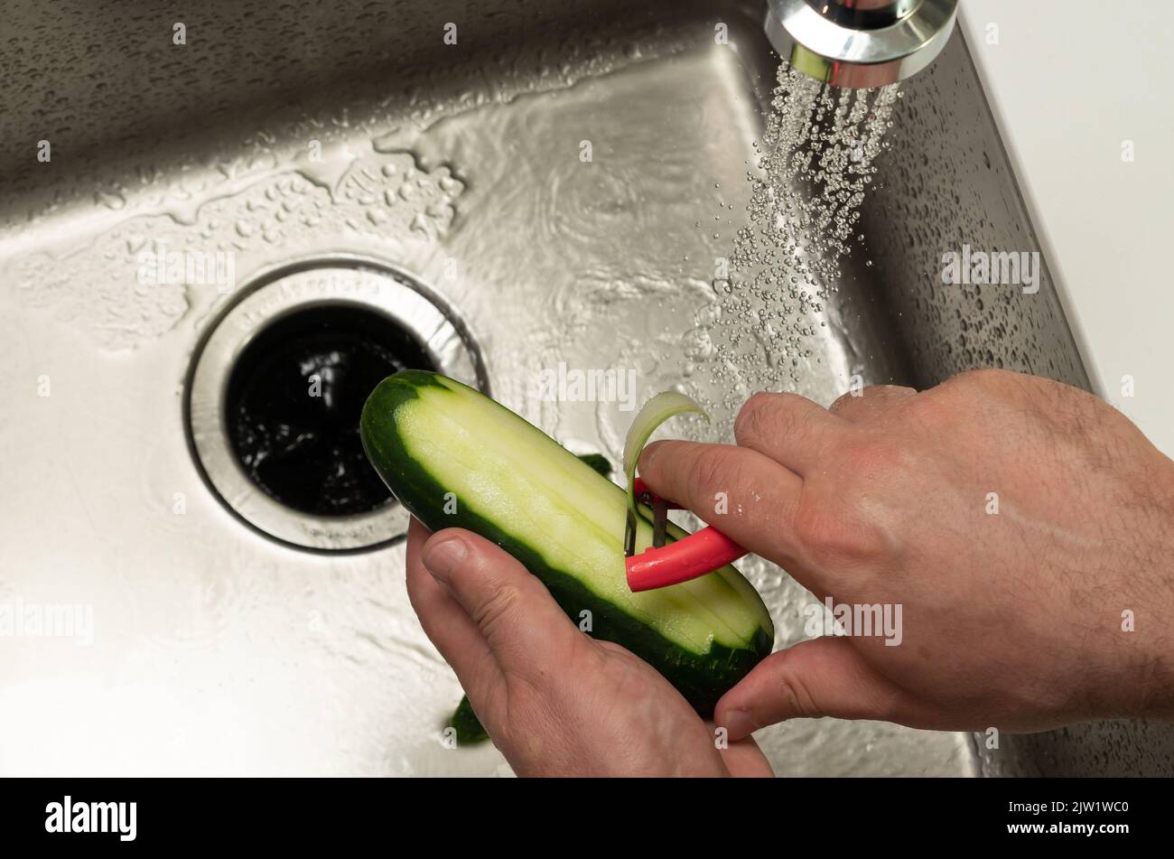 Halbgeschälte Gurke über dem Waschbecken in männlichen Händen Draufsicht Stockfoto