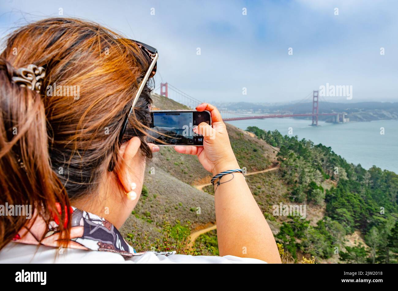 Eine Dame fotografiert die Golden Gate Bridge auf ihrem Handy während ihres Urlaubs in San Francisco, Kalifornien, USA Stockfoto