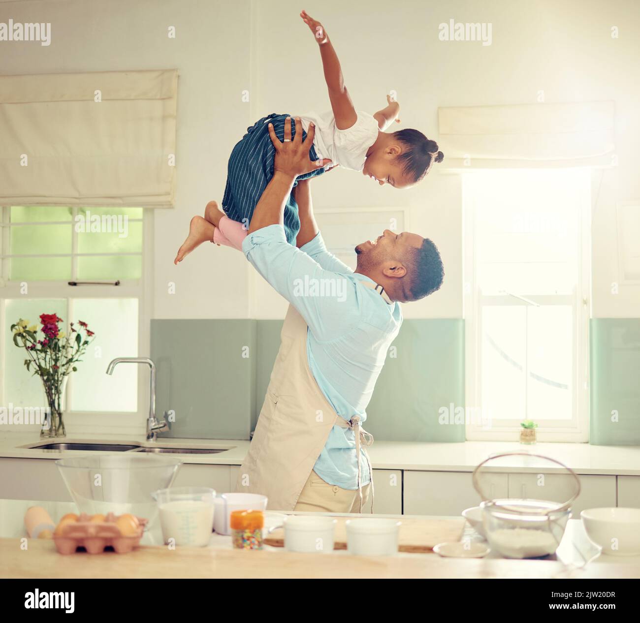 Glücklicher schwarzer Vater und Tochter, die in einer Küche spielen, während sie zusammen kochen, sich verkleben und lachen. Afroamerikanische Eltern genießen die Zeit mit der Familie Stockfoto