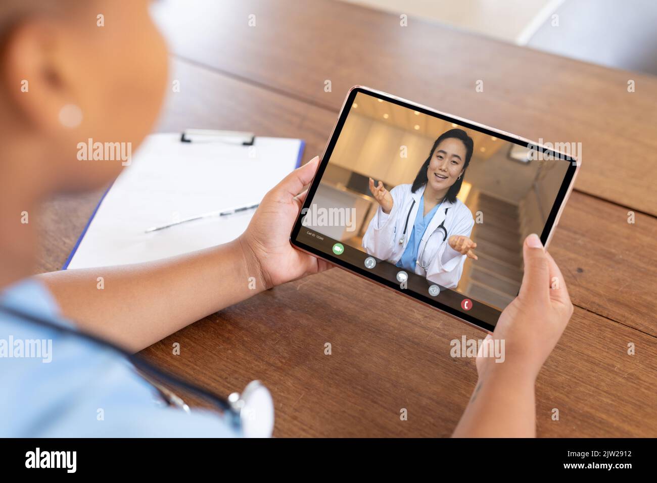 Lächelnde asiatische Ärztin, die während eines Videoanrufs mit einer afroamerikanischen Kollegin gestikuliert Stockfoto