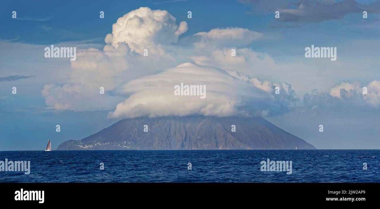 Segelschiff vor Vulkan Stromboli und Insel mit bizarrer Wolkenlandschaft, Stromboli, Kalabrien, Italien Stockfoto